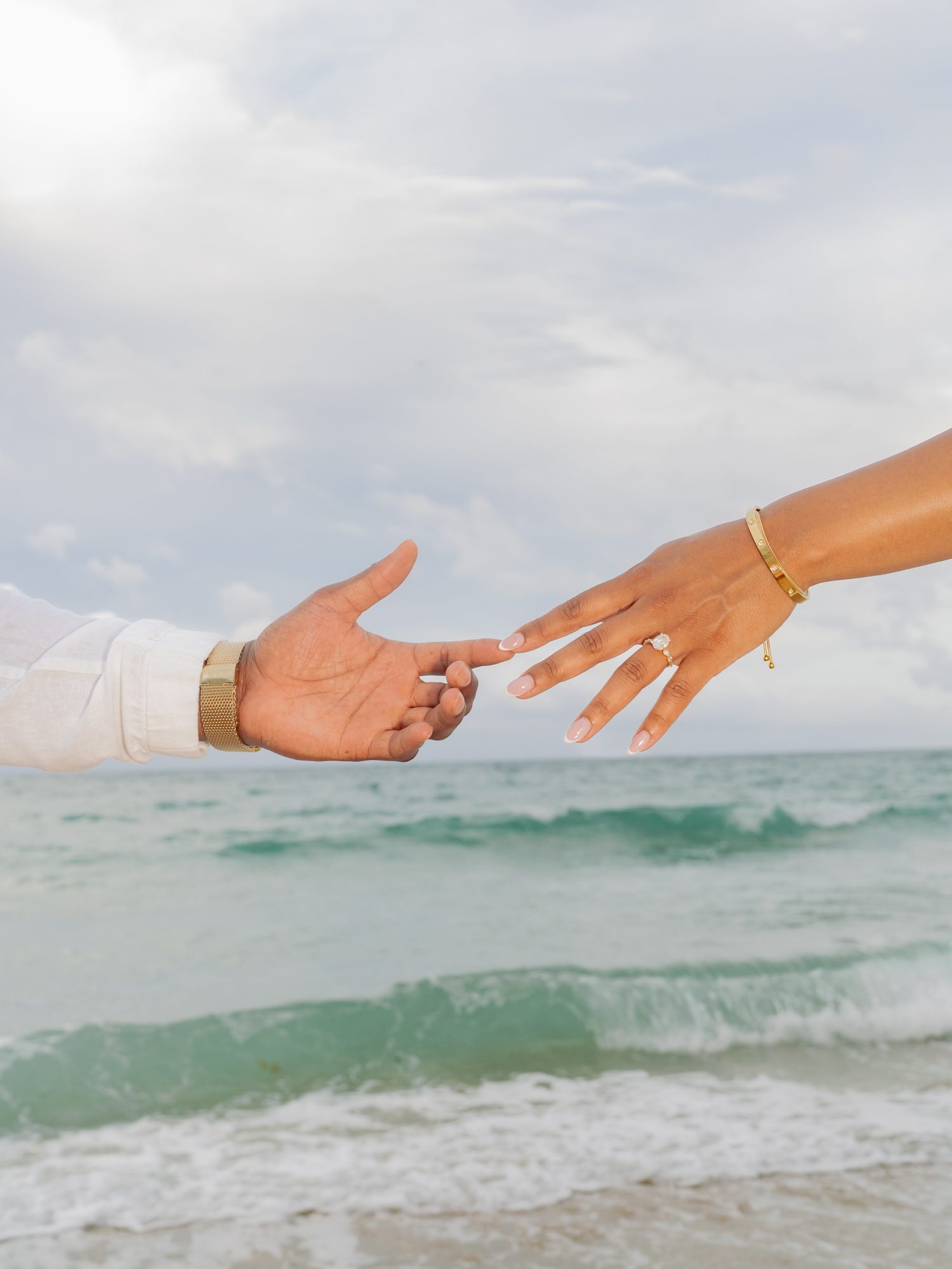 Clasped hands with an engagement ring near ocean waves