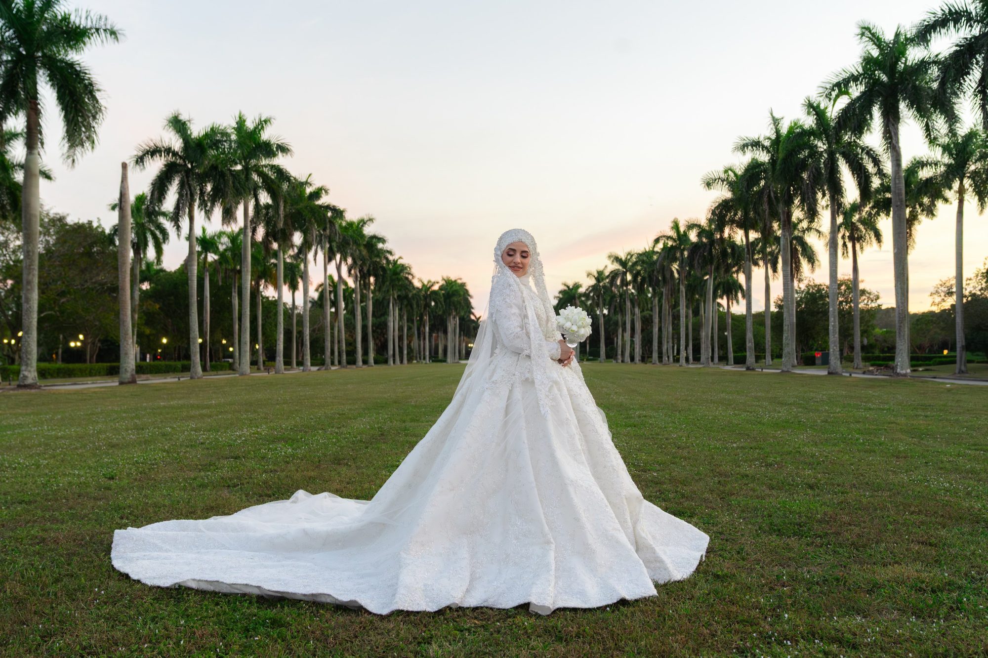 Bride standing alone in a palm lined garden walkway at sunset
