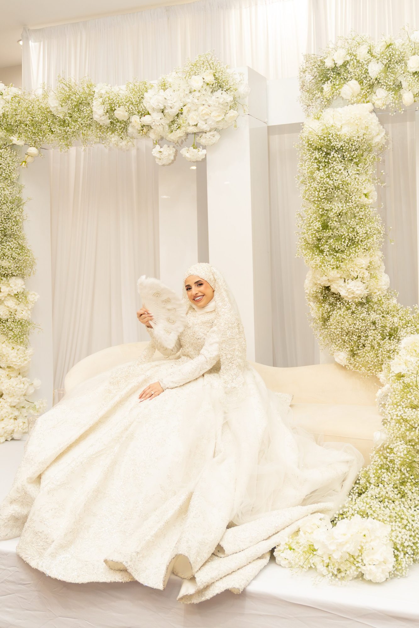 Bride in a beaded gown seated under a floral arch
