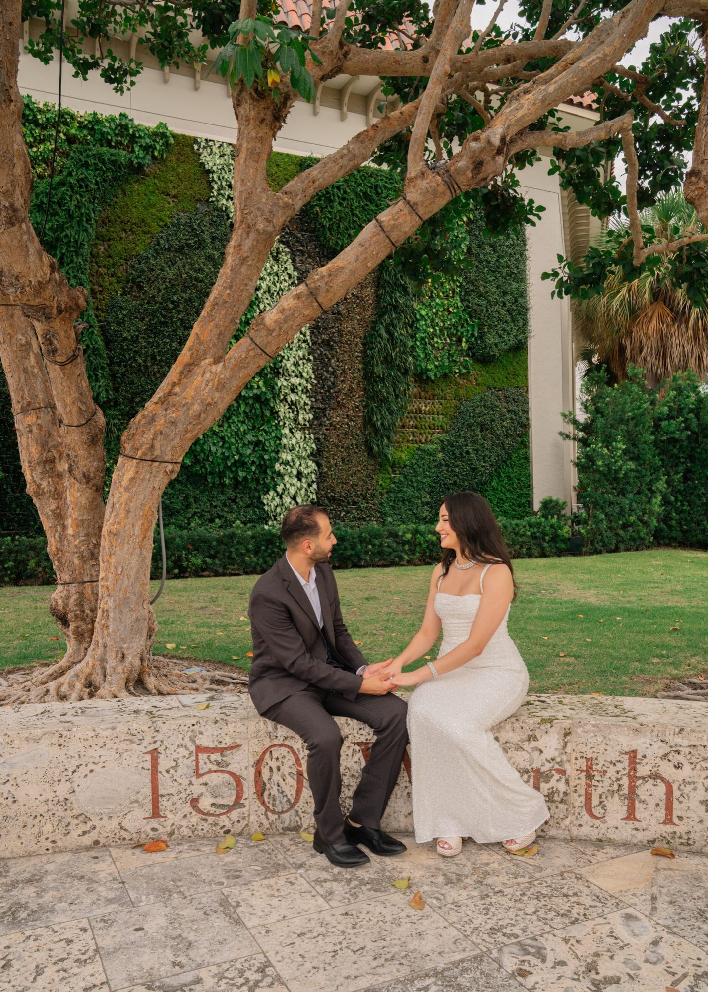 Couple sitting together on a stone wall under a tree