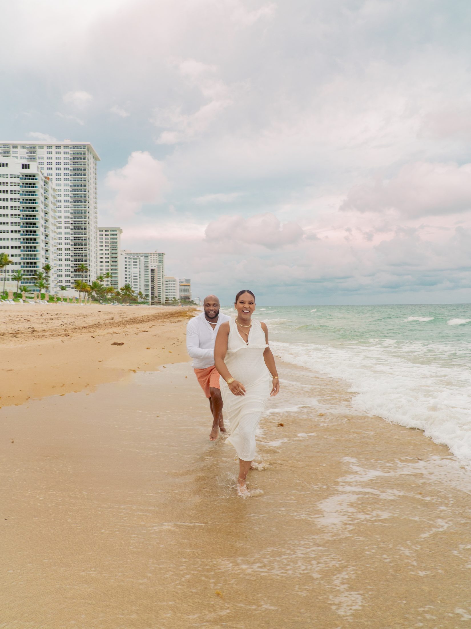 Couple walking the surf in Fort Lauderdale with the beachfront skyline behind them