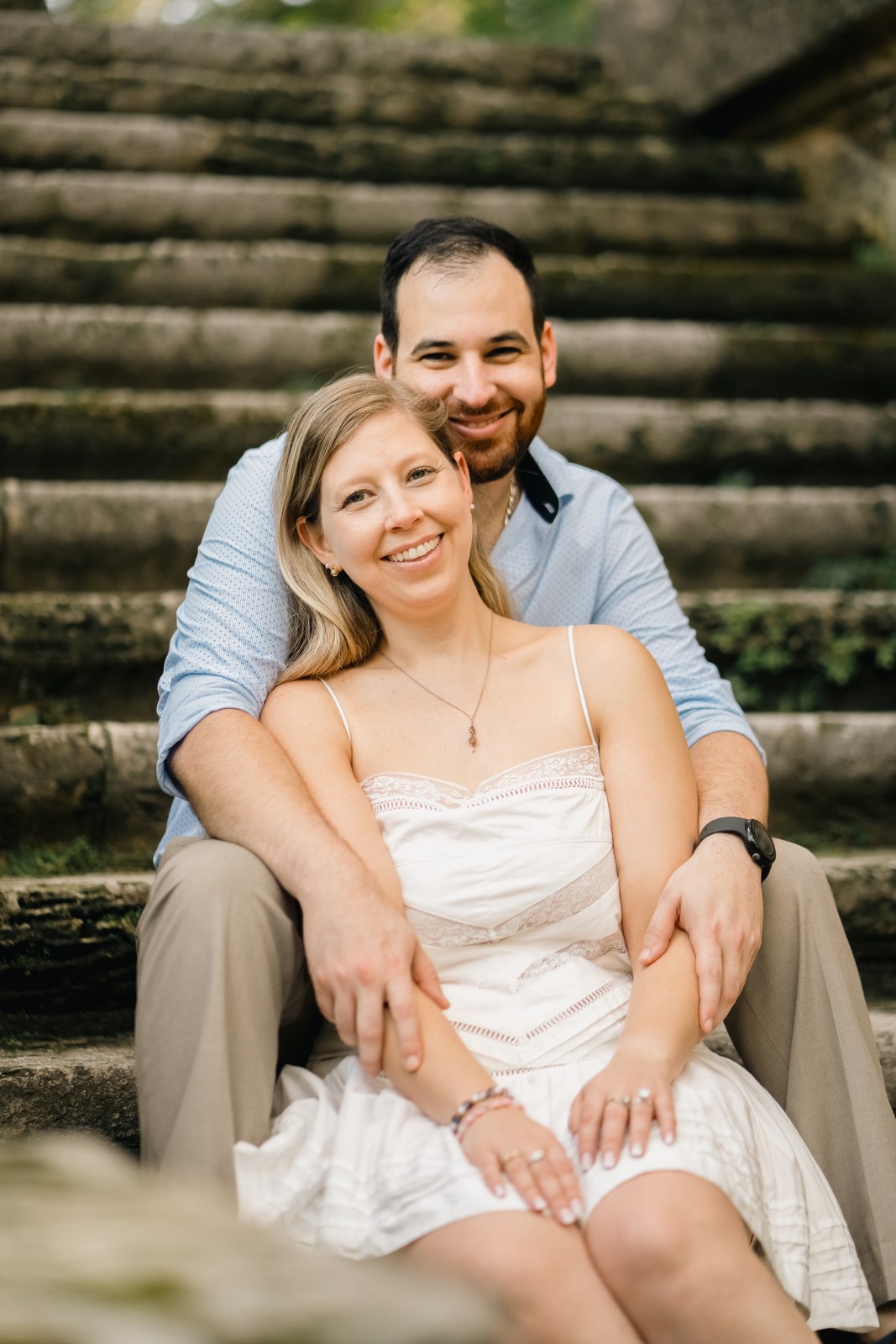 Groom smiling with the bride nestled close beside him on a garden bench