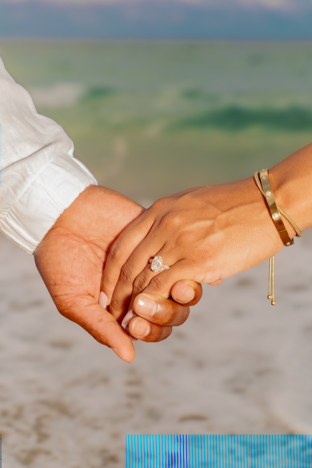 Couple holding hands on the beach with their rings in view
