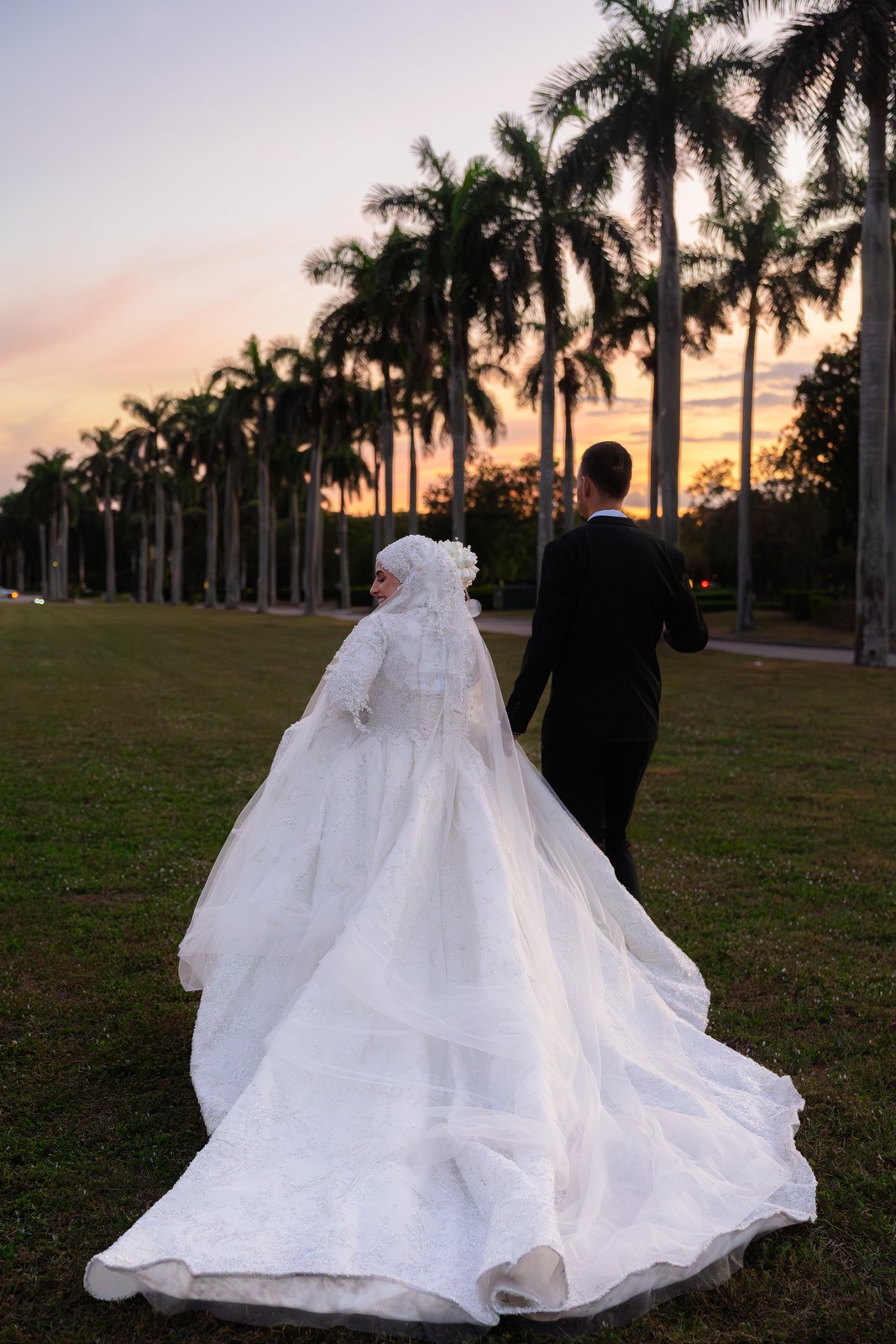 Bride and groom walking away down a palm lined path at sunset