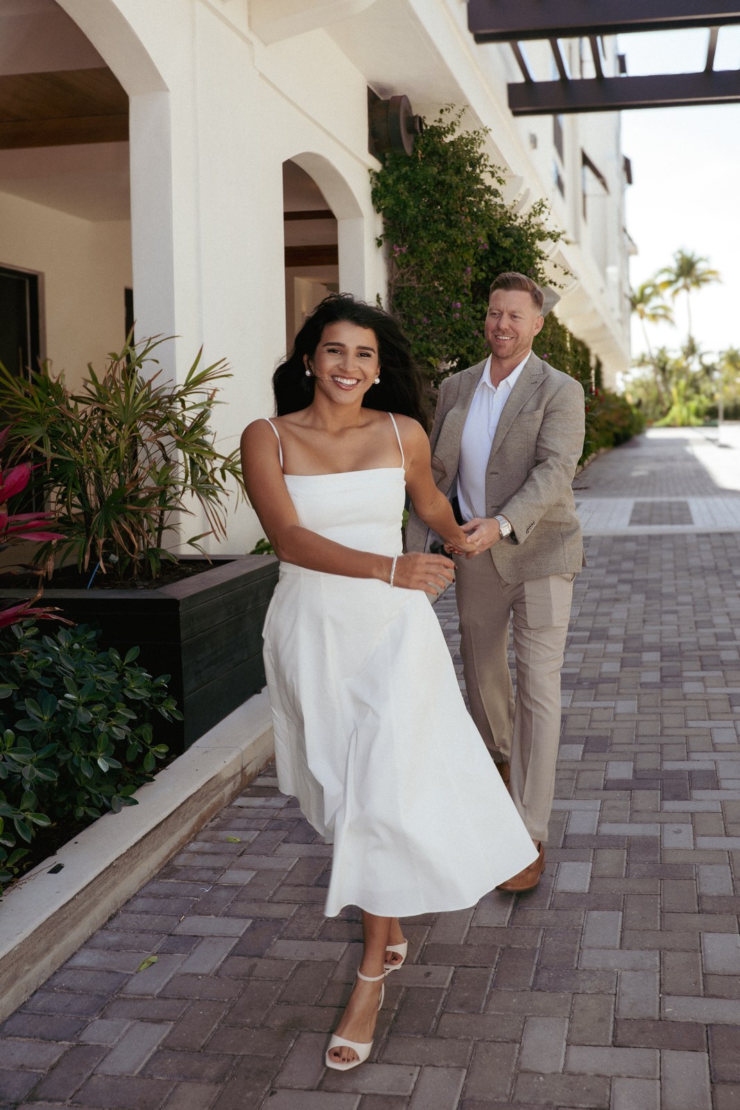 Bride walking a resort promenade with the groom just behind