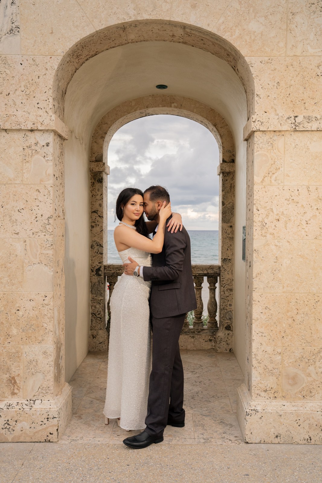 Couple embracing under a stone archway with the ocean behind them